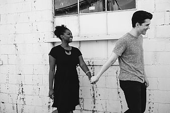 Black and white photo of a happy couple holding hands walking past a wall