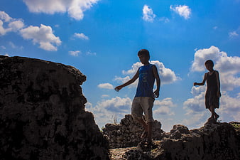 Two boys playing on rocks against blue sky