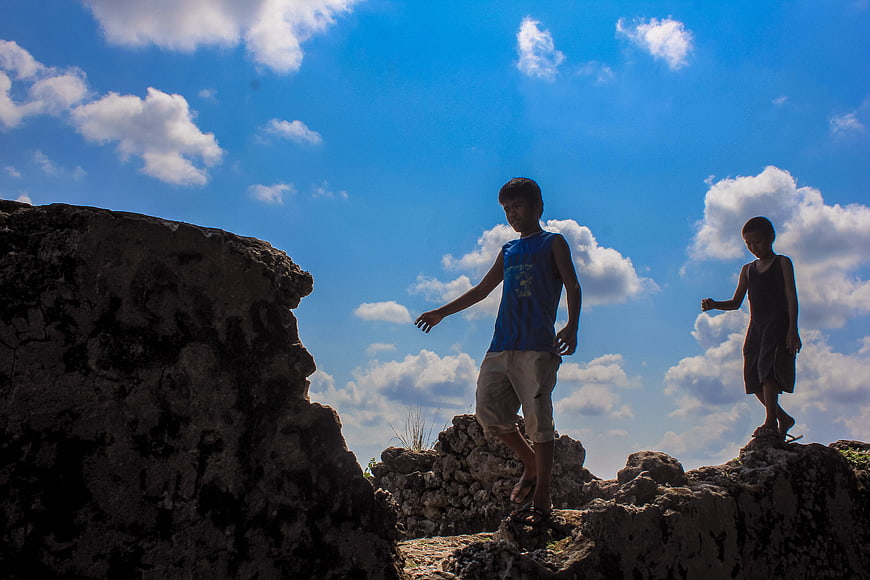 Two boys playing on rocks against blue sky