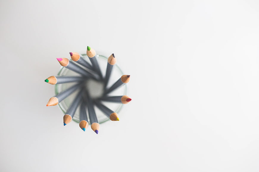 Top view of colored pencils in a glass jar on white background