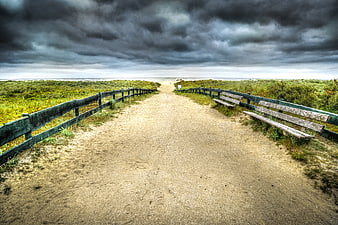 Sandy path to beach under dramatic storm clouds