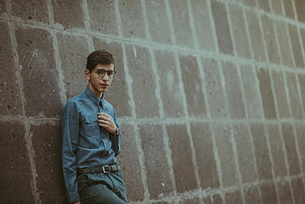 Young man with glasses leaning against concrete wall