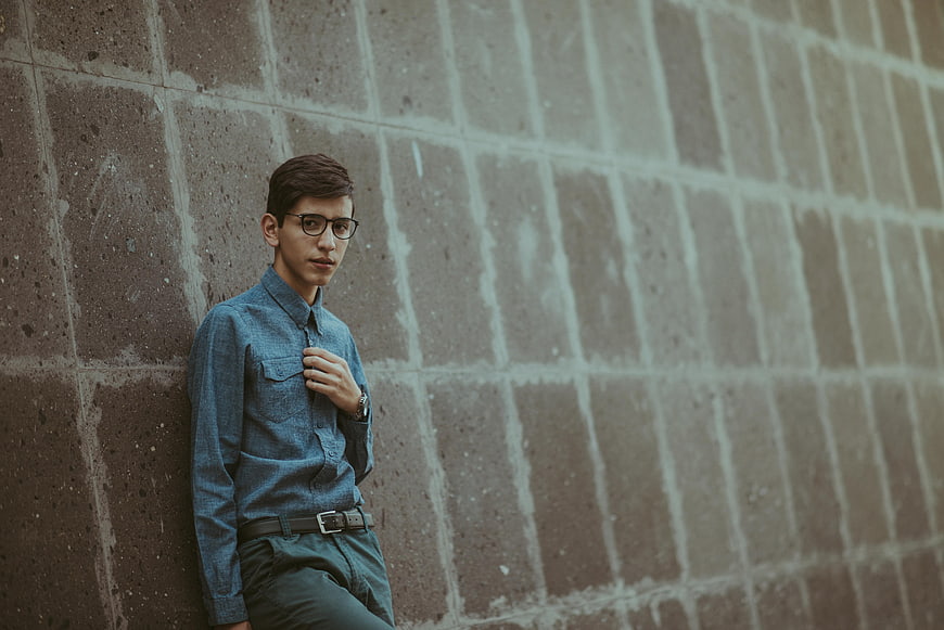 Young man with glasses leaning against concrete wall