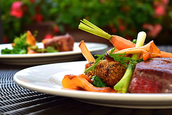 Gourmet plated meal with steak, vegetables, and fresh herbs on a white plate