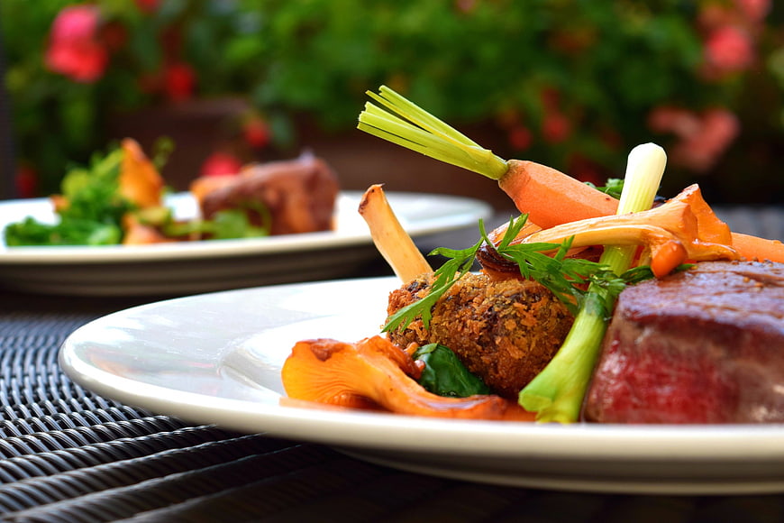 Gourmet plated meal with steak, vegetables, and fresh herbs on a white plate