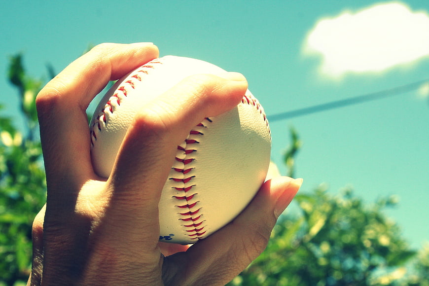 Hand Holding Baseball Against Blue Sky