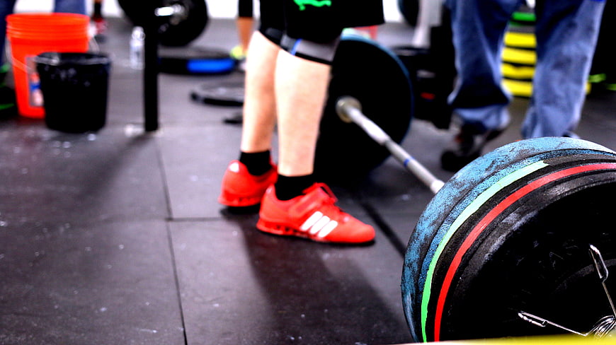 Athlete lifting barbell in gym with red sneakers