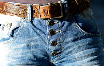 Close-up of blue denim button fly jeans with brown belt