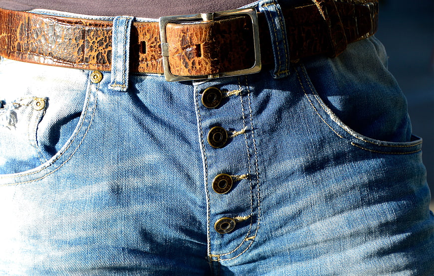 Close-up of blue denim button fly jeans with brown belt