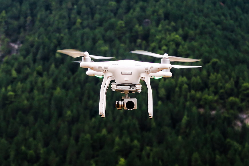 White drone flying over green forest background
