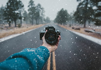 Hand holding vintage Nikon camera on snowy road