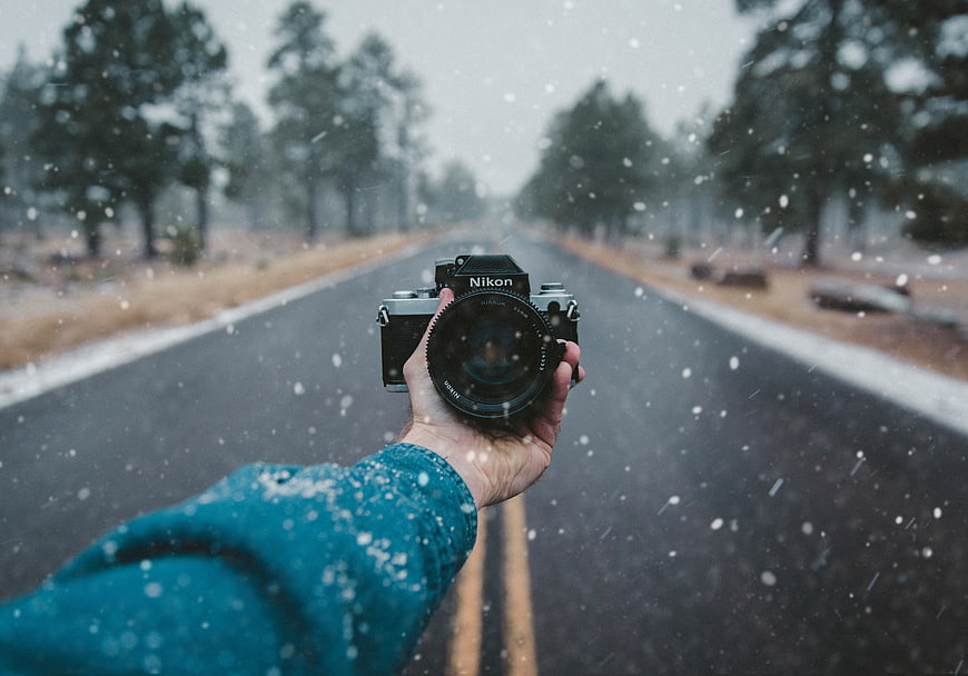 Hand holding vintage Nikon camera on snowy road