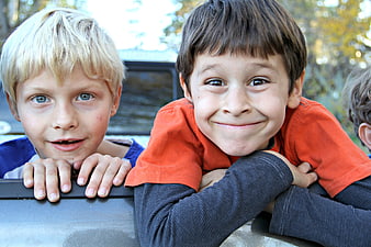 Two smiling young boys leaning on a car outdoors