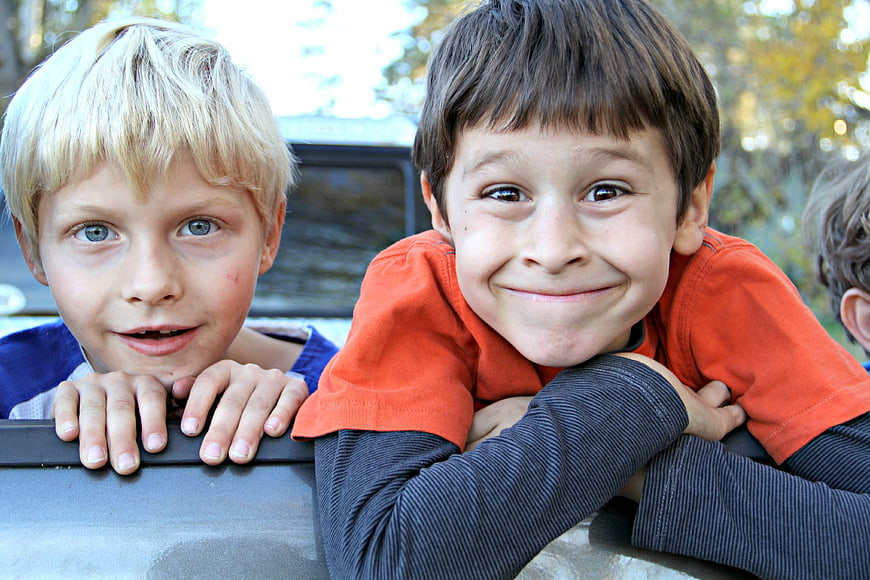 Two smiling young boys leaning on a car outdoors
