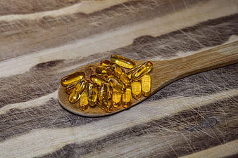 Yellow Fish Oil Capsules on Wooden Spoon