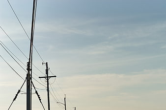 Silhouette of power lines and utility poles against blue sky