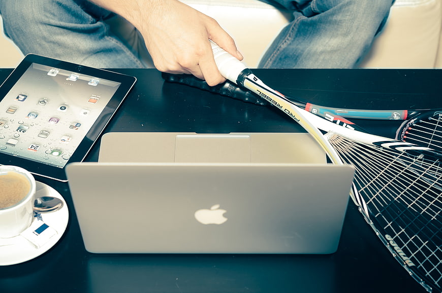 Tennis racket, laptop, tablet, and coffee on a table