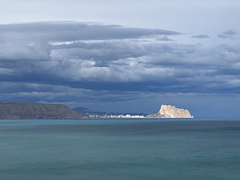Dramatic view of Ifach Rock and Calpe coastline under cloudy sky