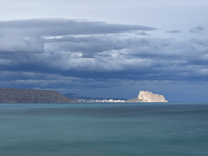 Dramatic view of Ifach Rock and Calpe coastline under cloudy sky