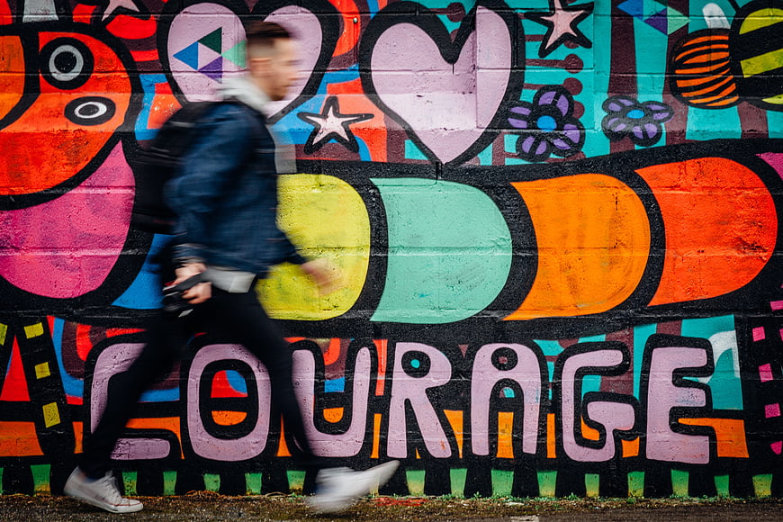 Motion blur man walking past colorful street art mural with courage text