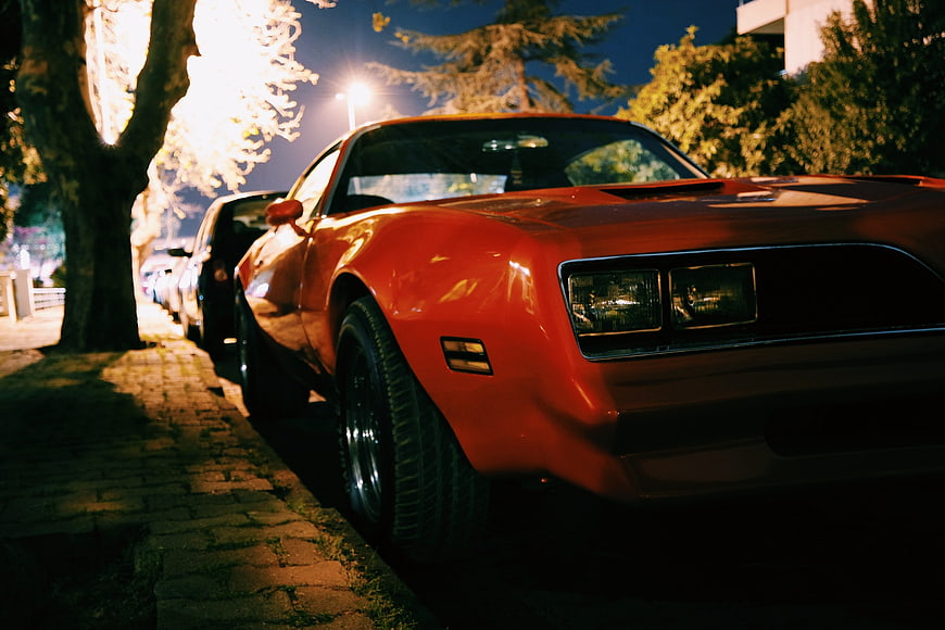 Red Classic Muscle Car Parked on Cobblestone Street at Night