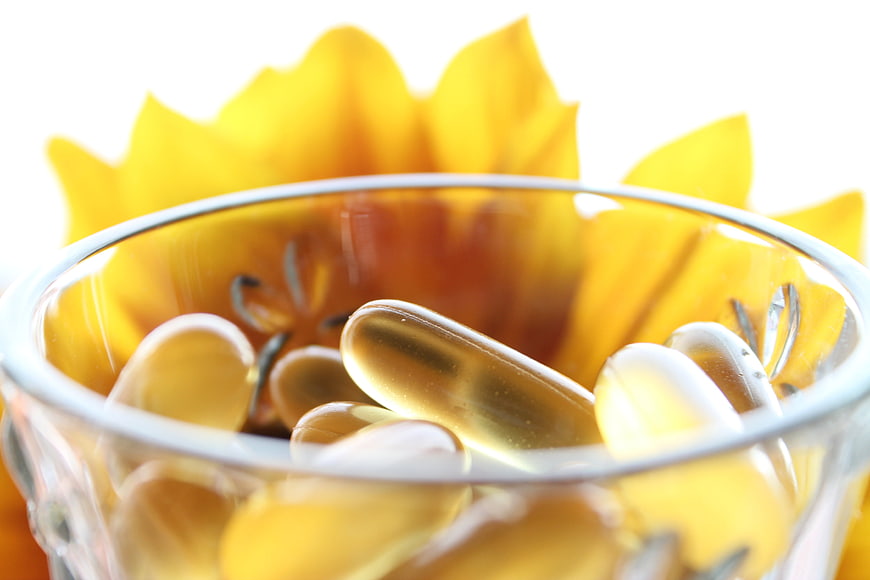 Golden Fish Oil Capsules in Glass Bowl with Sunflower