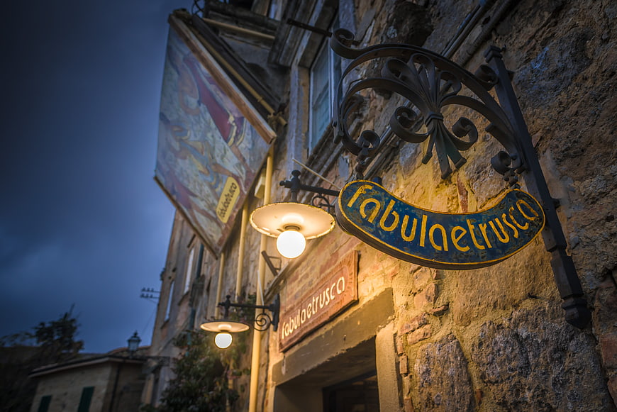 Illuminated Fabula Etrusca sign on historic stone building facade