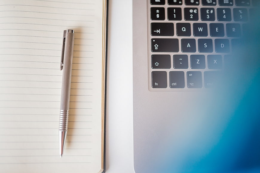 Silver pen on notebook next to laptop keyboard