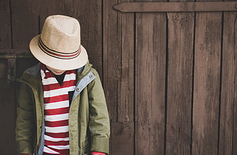 Young boy in straw hat and striped shirt against wooden wall
