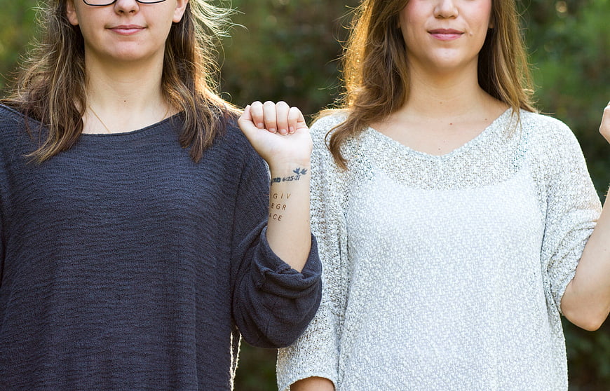 Two women raising fists with solidarity tattoo on wrist