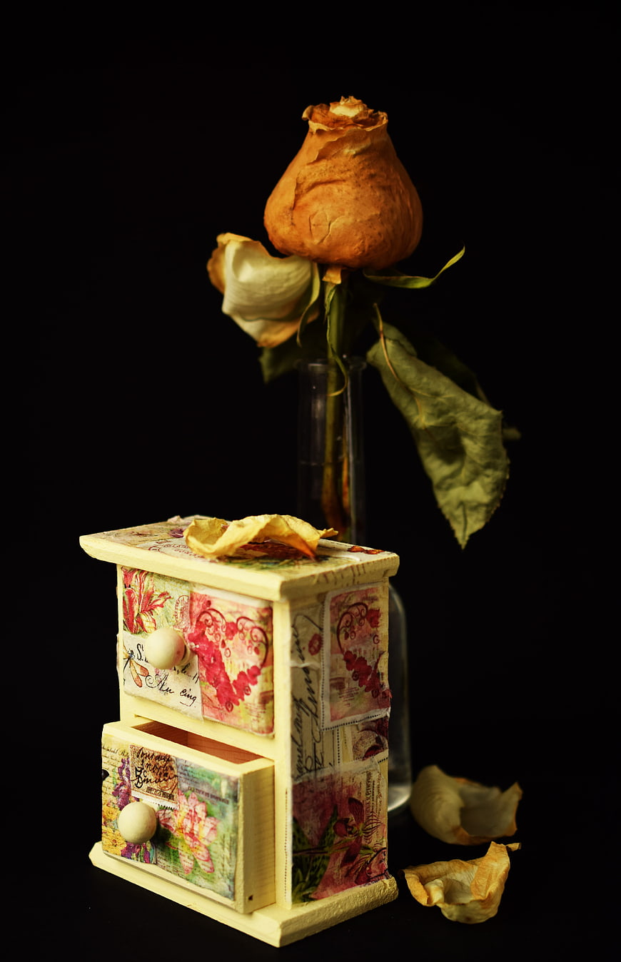 Vintage miniature cabinet with dried rose on black background