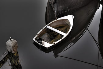 Small white dinghy tied to large dark ship in calm water
