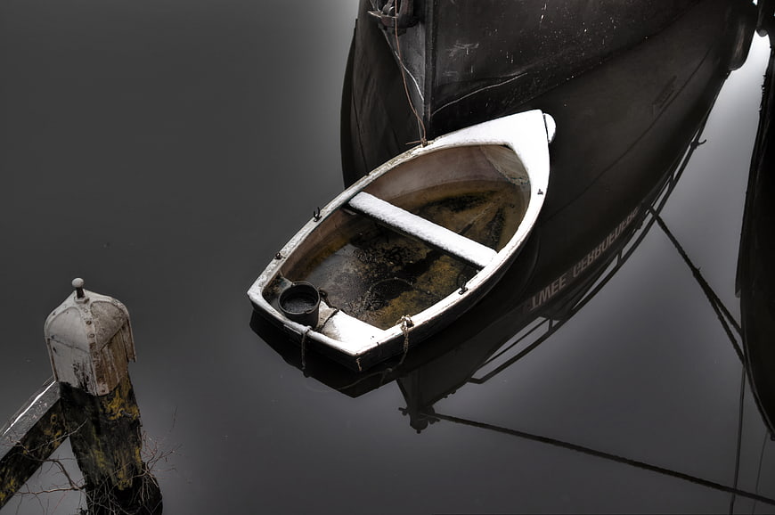 Small white dinghy tied to large dark ship in calm water