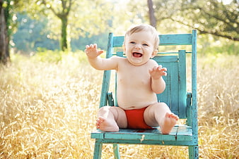 Happy baby boy sitting on blue chair in sunny field