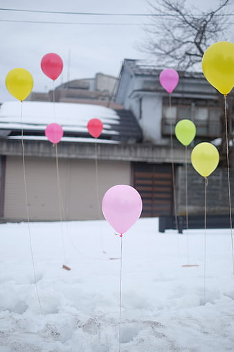 Colorful balloons stuck in snow outside a house