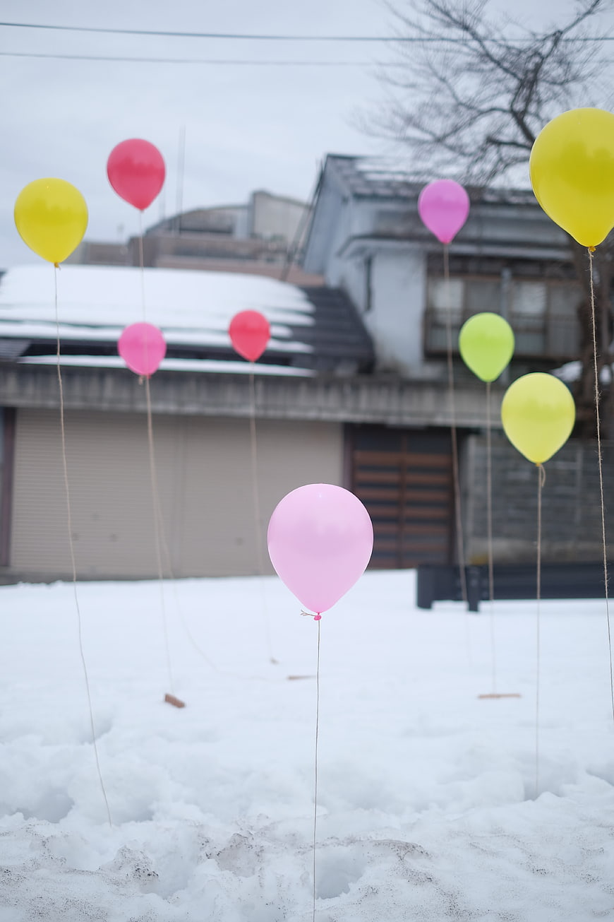 Colorful balloons stuck in snow outside a house