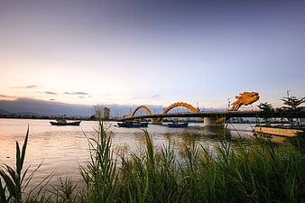 Dragon Bridge in Da Nam, Vietnam at sunset with river boats and foreground grass