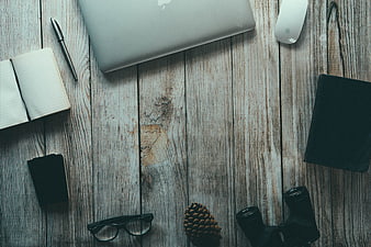 Flat lay workspace with laptop, notebook, and binoculars on wood