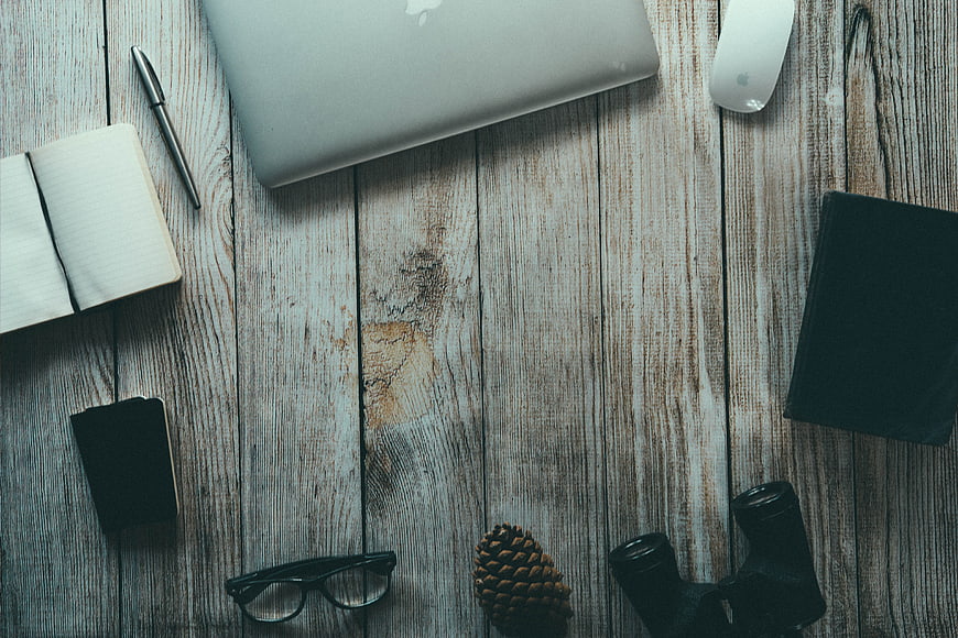 Flat lay workspace with laptop, notebook, and binoculars on wood