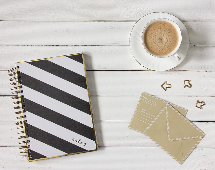 Flat lay of striped notebook, coffee cup, and envelopes on white wood