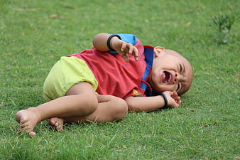 Crying baby boy lying on green grass