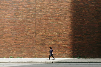 Woman walking past a large textured red brick wall on a city street
