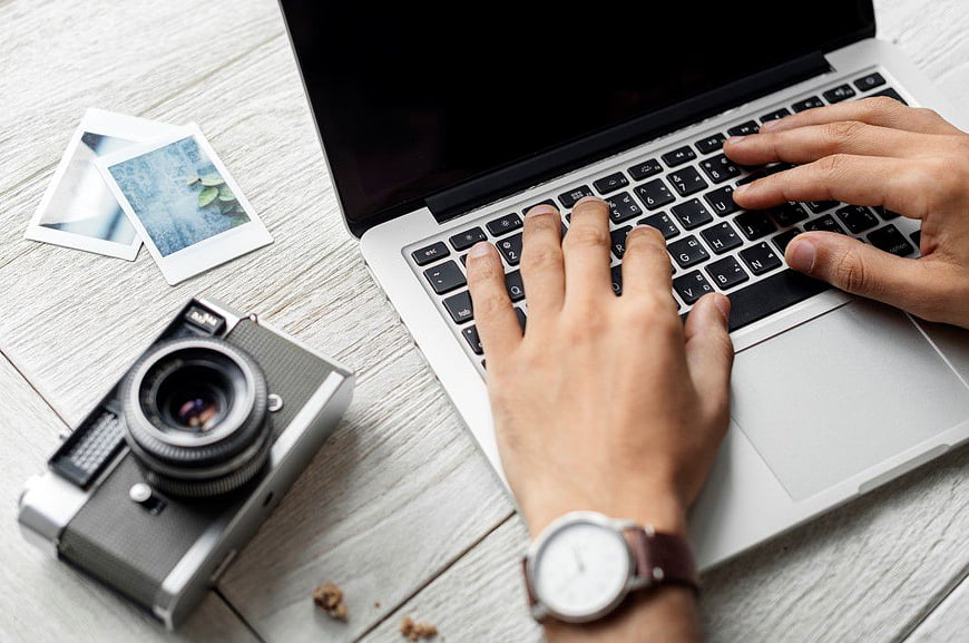 Photographer Typing on Laptop with Vintage Camera and Prints