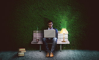 Man working on laptop on park bench at night with lamp
