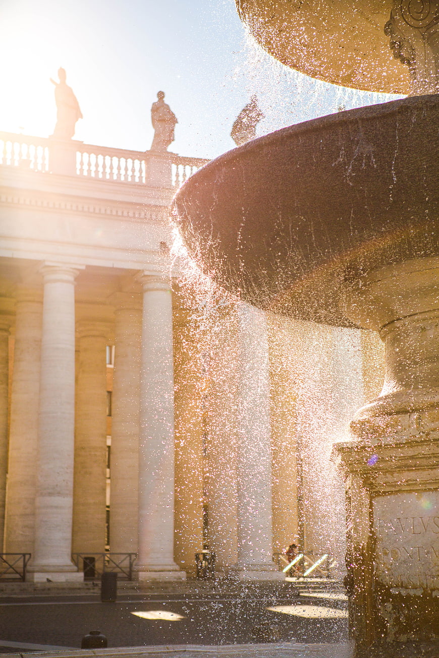 Sunlit Fountain Spray In Front Of Classical Roman Architecture
