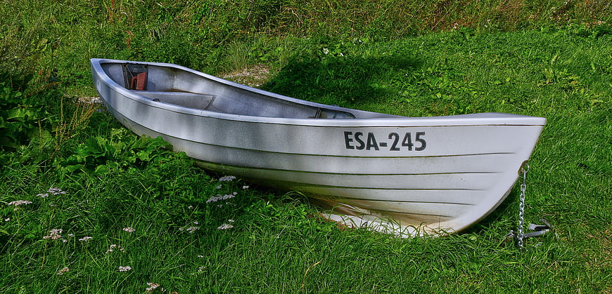 Silver aluminum boat resting on green grass with anchor