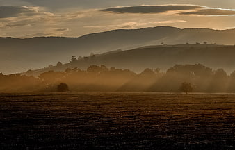 Misty Sunrise Over Rolling Hills With Golden Light Rays