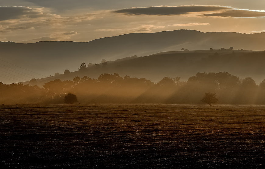 Misty Sunrise Over Rolling Hills With Golden Light Rays