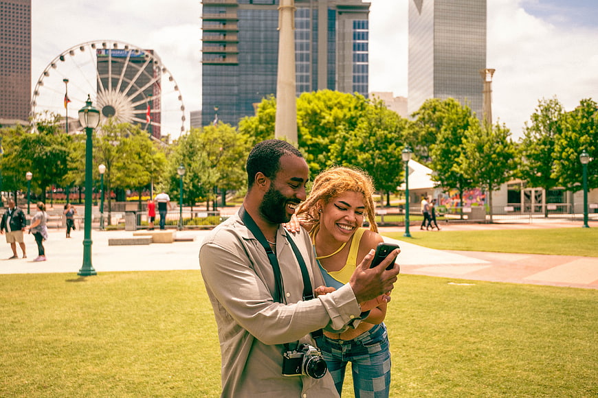 Happy Diverse Couple Looking at Smartphone in City Park