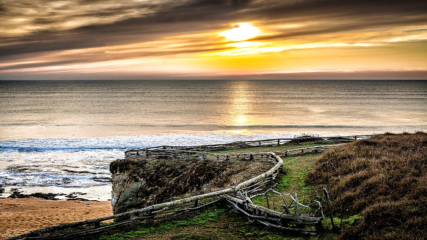 Dramatic Sunset Over Ocean with Rustic Wooden Fence